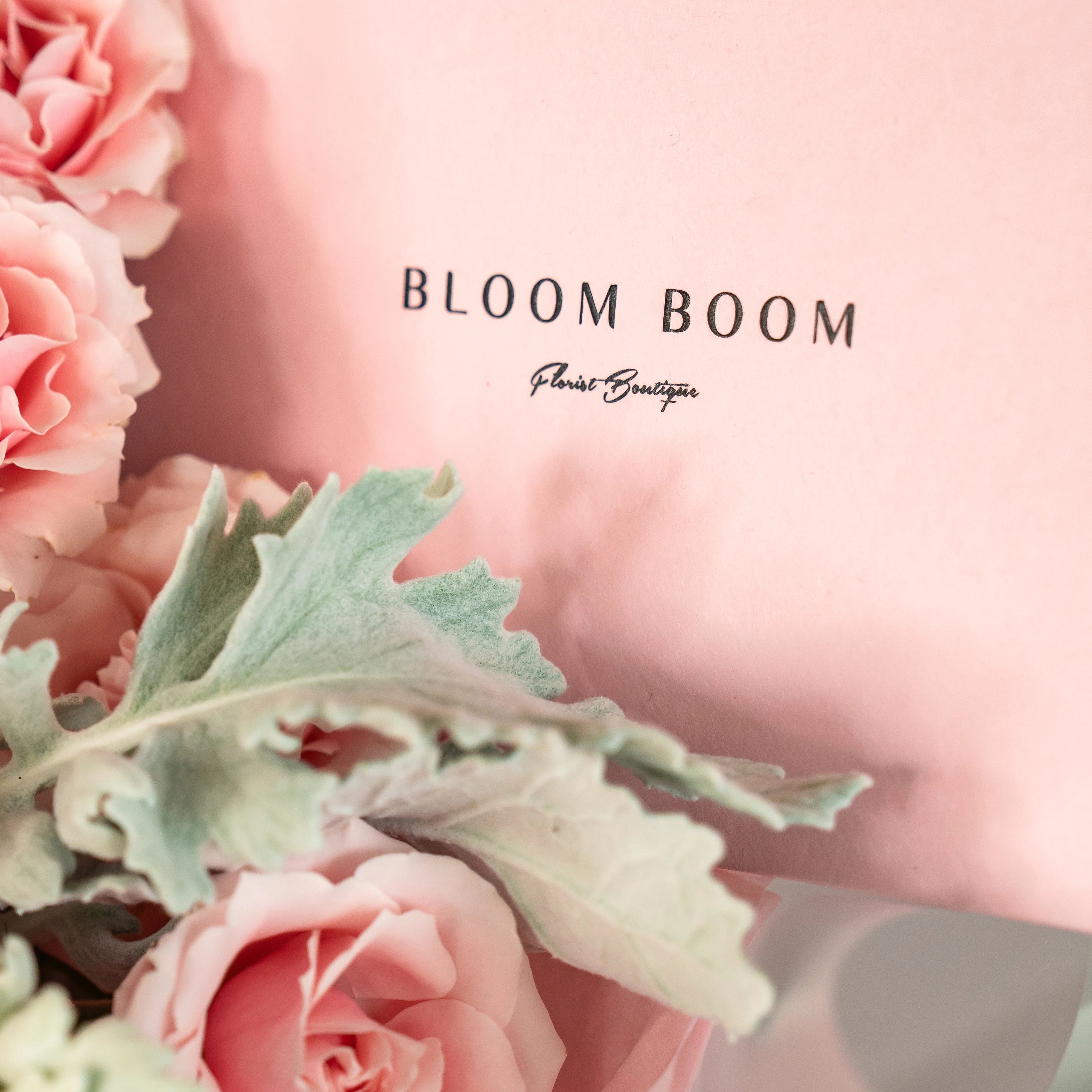 Bloom Boom Florist Boutique logo with coral pink roses and dusty miller greenery on soft pink background