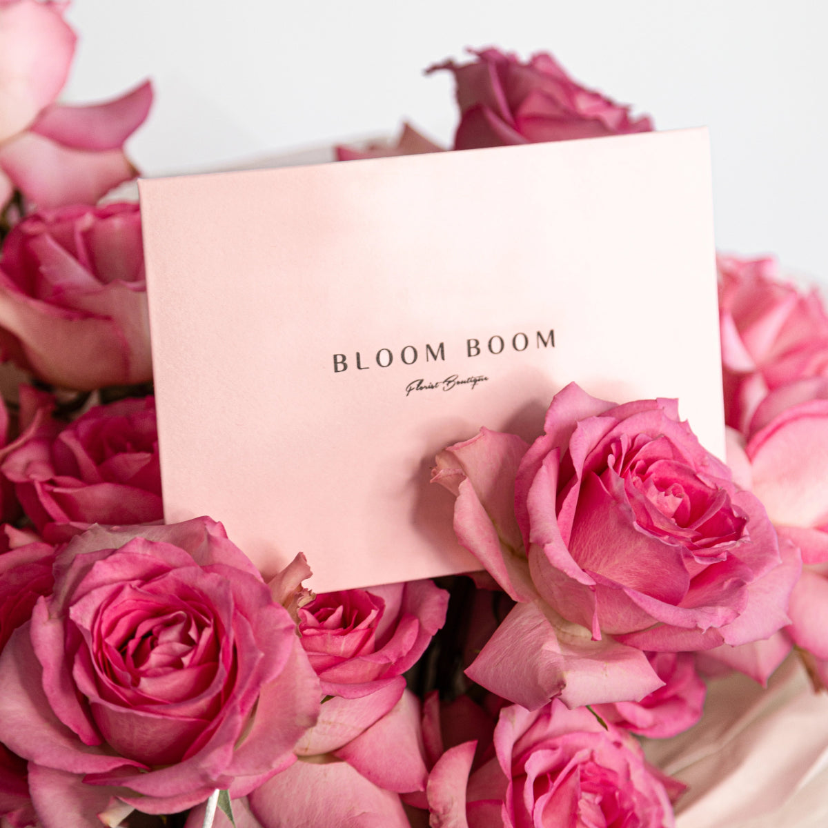 Pink Bloom Boom gift card nestled in bouquet of soft pink roses with elegant white packaging