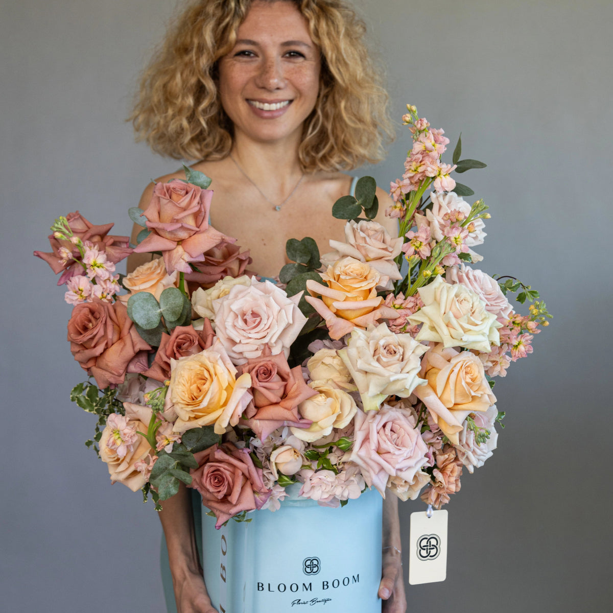 Luxury pastel rose bouquet in blue Bloom Boom hatbox with peach, pink, and cream roses plus eucalyptus leaves