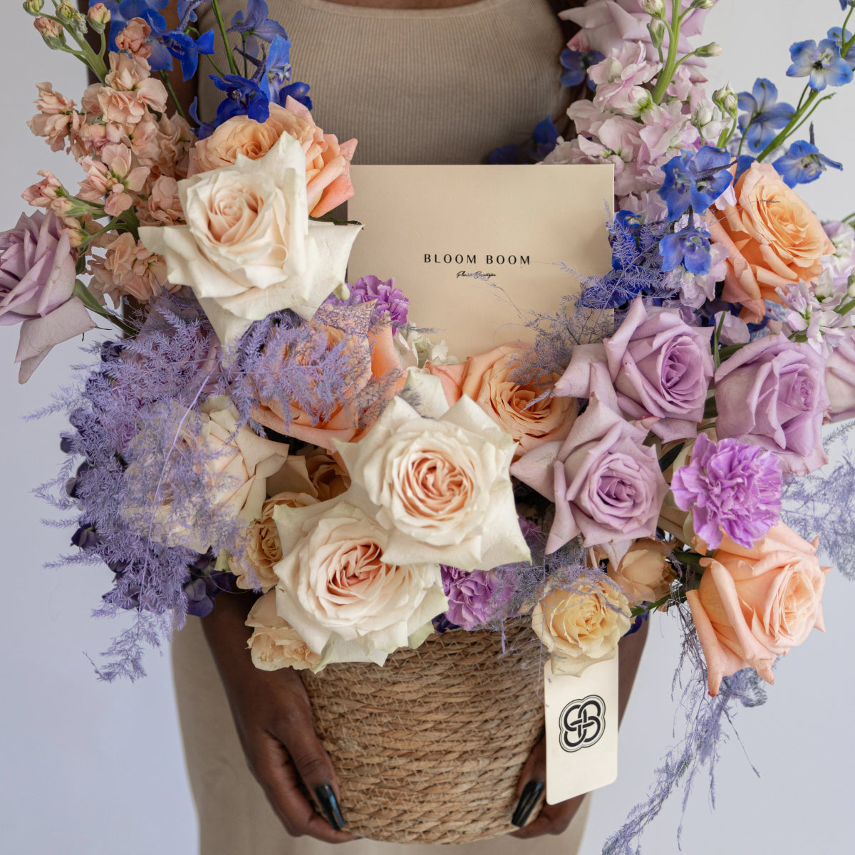 Wicker basket flower arrangement with cream roses, purple hydrangeas, peach roses and blue delphiniums