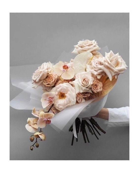Elegant bridal bouquet with blush pink roses, white orchids, and cream flowers wrapped in white ribbon
