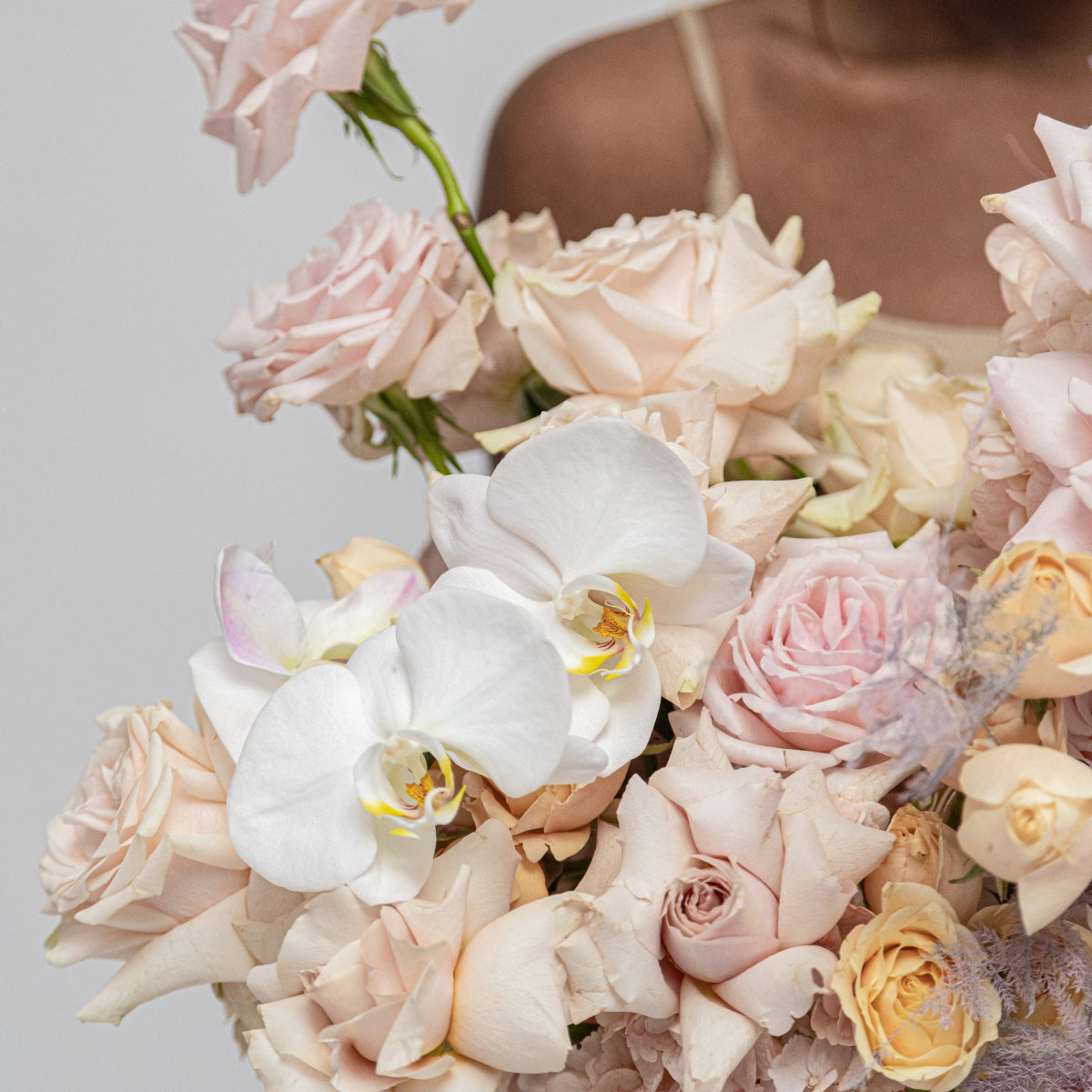 Elegant floral bouquet with white orchids, blush pink roses, and cream flowers in soft pastel arrangement