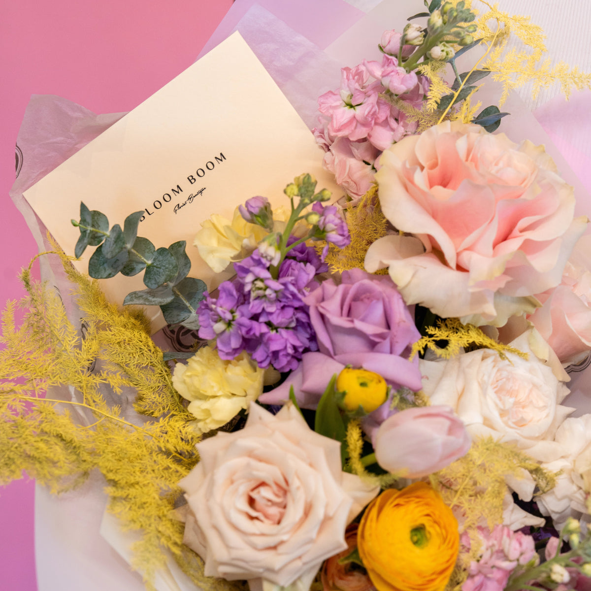 Pastel flower bouquet with pink roses, purple stock, yellow ranunculus, eucalyptus and golden mimosa