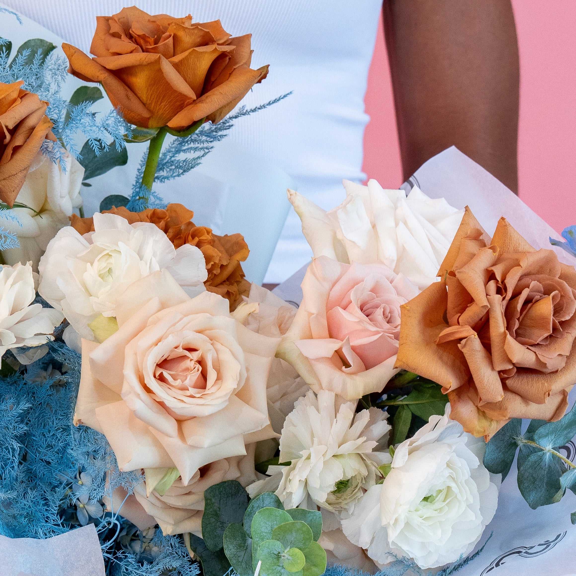 Cappuccino and blush pink rose bouquet with white ranunculus and blue dusty miller foliage wrapped in paper