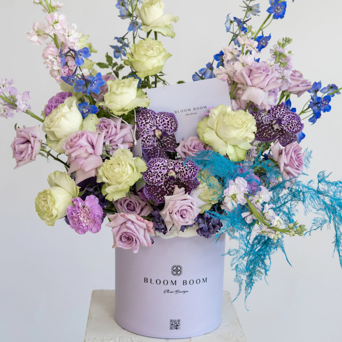 Luxurious floral arrangement with purple roses, white roses, orchids and blue delphinium in lavender round gift box