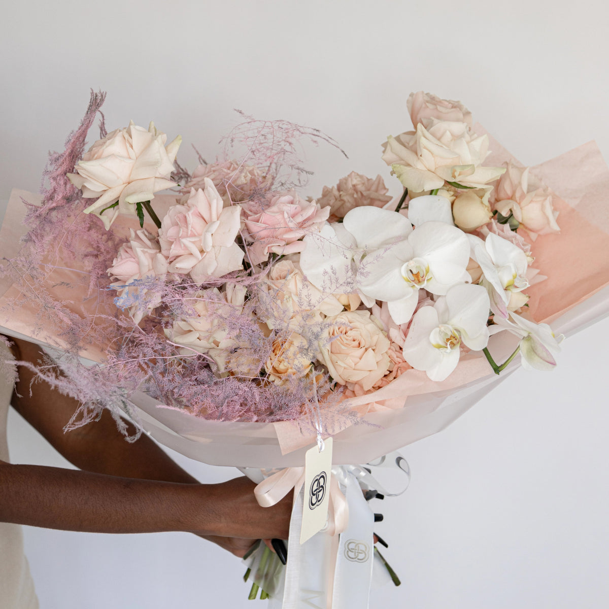 Pastel pink and white mixed flower bouquet with orchids, roses, and hydrangeas wrapped in mauve tulle