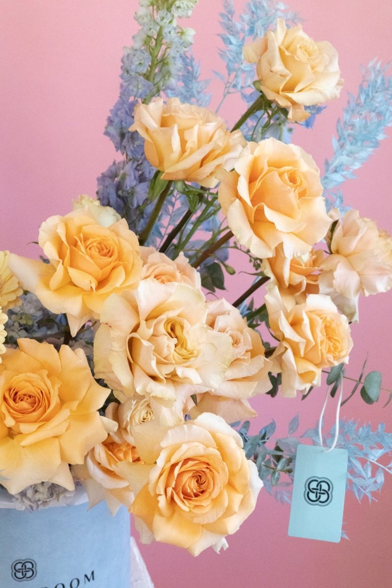 Peach and cream roses with blue dried flowers in elegant floral arrangement on pink background