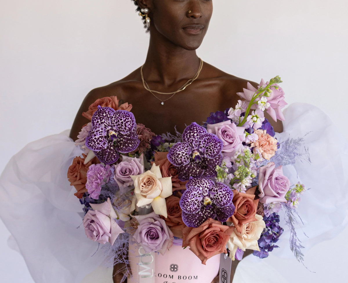 Purple spotted orchid bouquet with lavender roses, coral roses and white flowers in clear wrapping