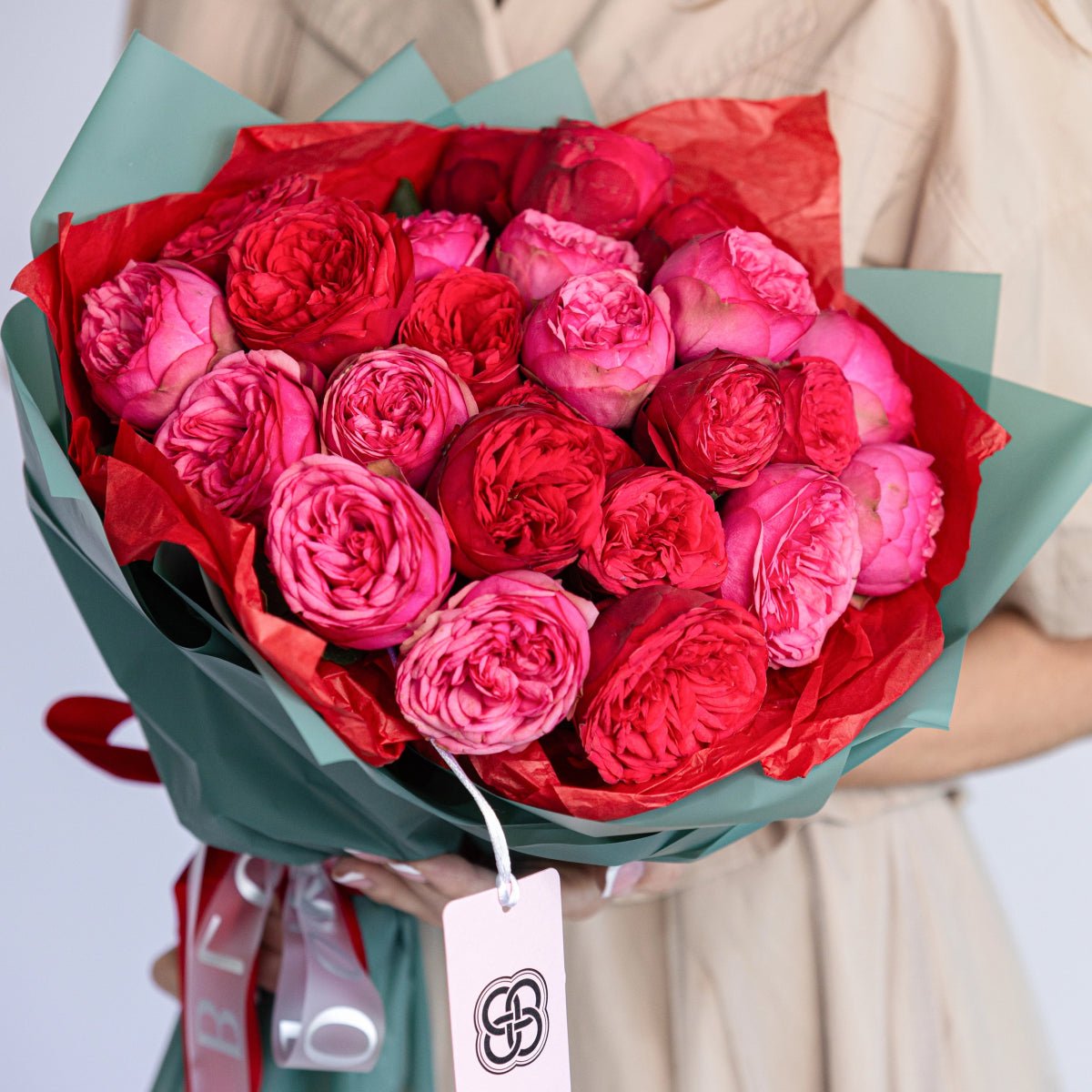 Luxury bouquet of red and pink garden roses with ruffled petals wrapped in mint green and red tissue paper