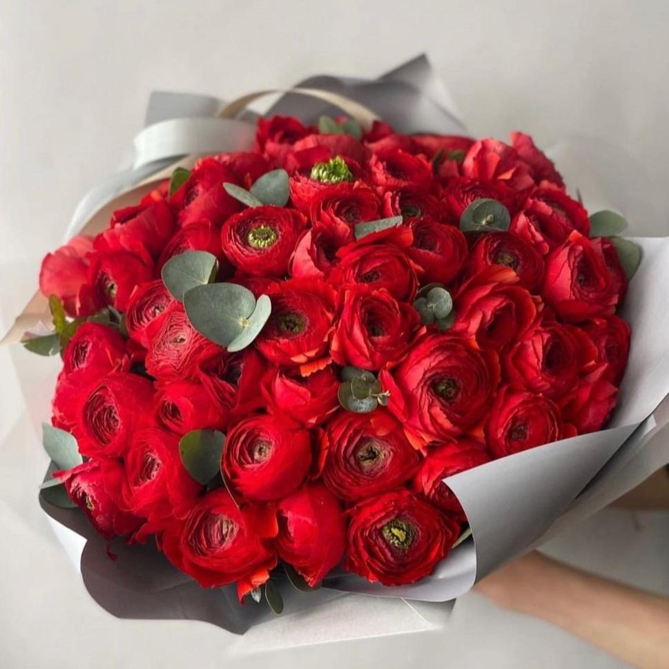 Vibrant red ranunculus bouquet with eucalyptus leaves wrapped in white and gray paper with ribbon