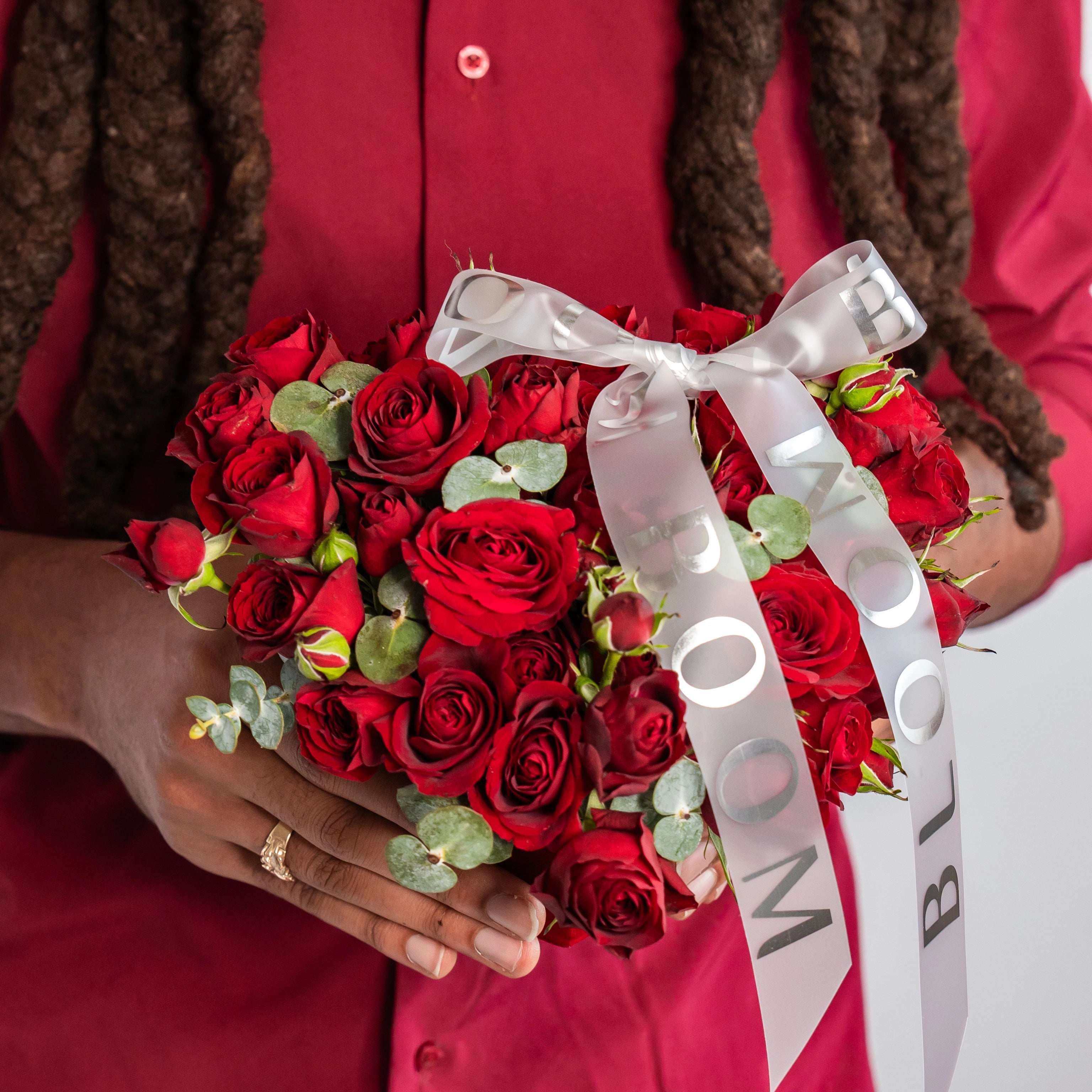 Red rose bouquet with eucalyptus greenery and white satin ribbon held by person in red outfit for Valentine's Day