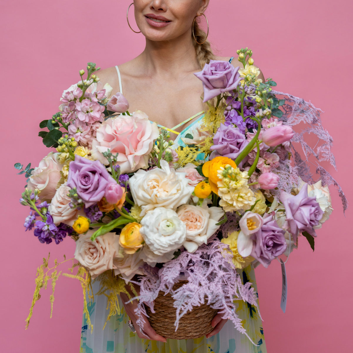 Colorful spring flower basket with purple roses, white ranunculus, yellow blooms and dusty miller in woven basket