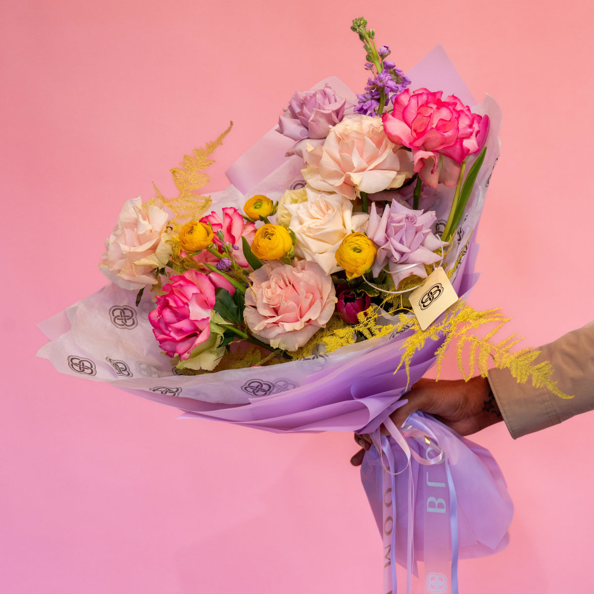 Colorful spring bouquet with pink peonies, cream roses, yellow ranunculus and purple flowers wrapped in lavender paper