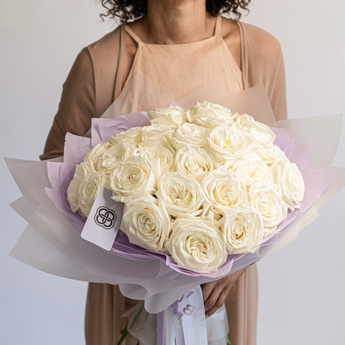 Luxury white rose bouquet wrapped in lavender tissue paper held by woman in beige dress