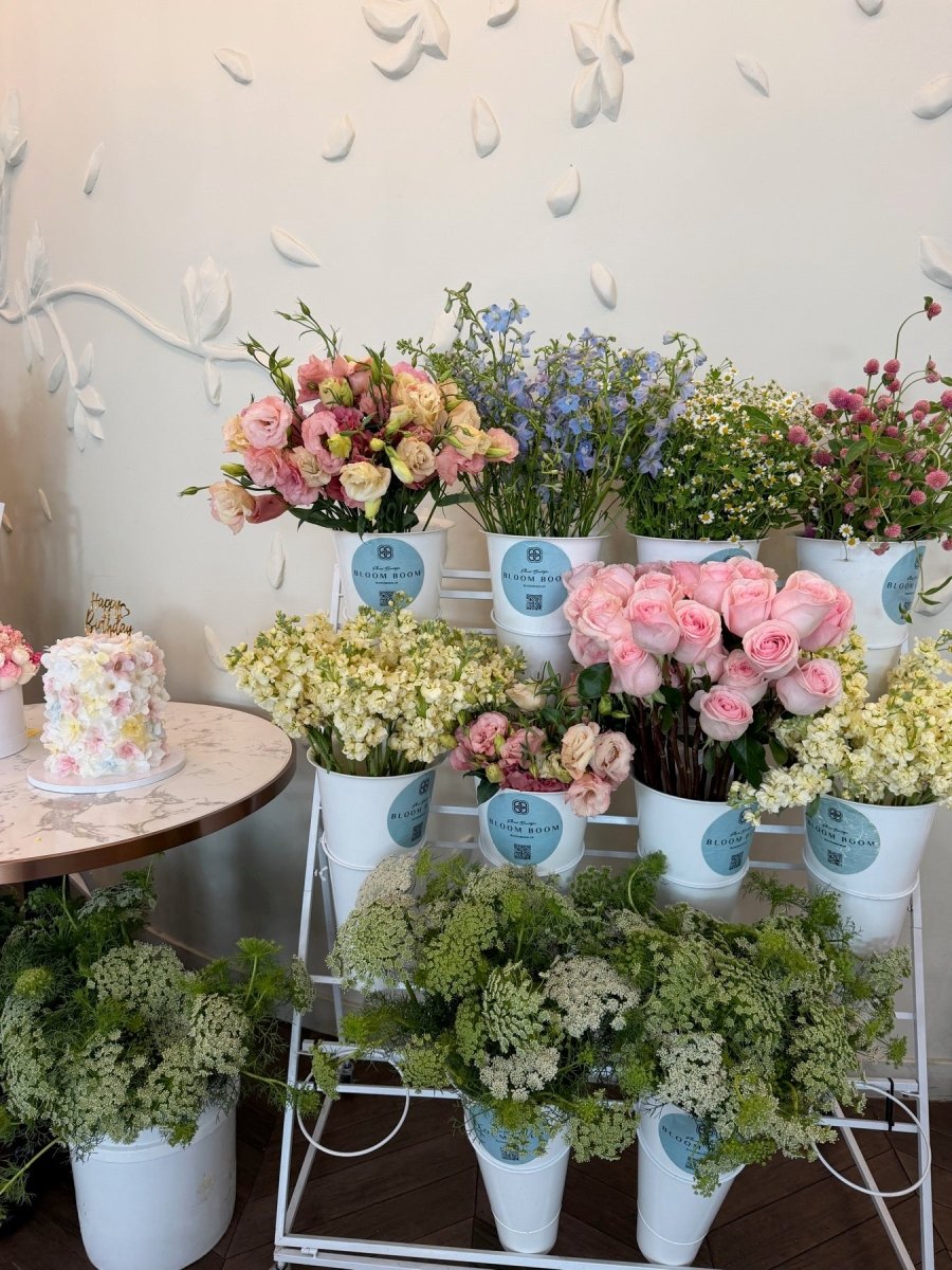 A Bloom Boom flower bar with seasonal pink, blue, cream, and green stems arranged in branded buckets.