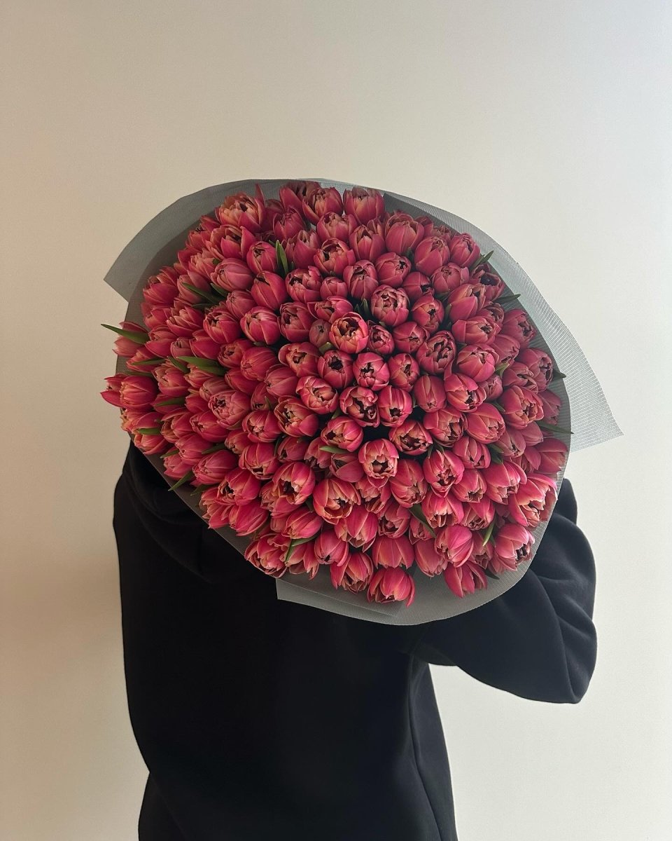 Large bouquet of 151 deep pink tulips wrapped in gray paper held by person in black clothing