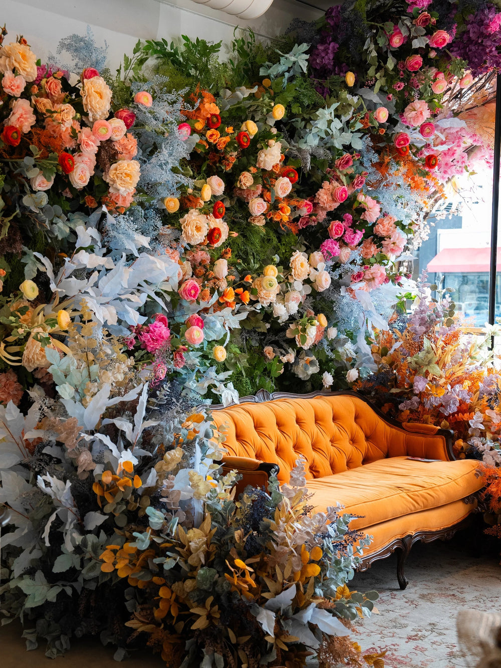 Orange velvet tufted sofa set against a floor-to-ceiling floral wall in coral, pink and pale blue blooms