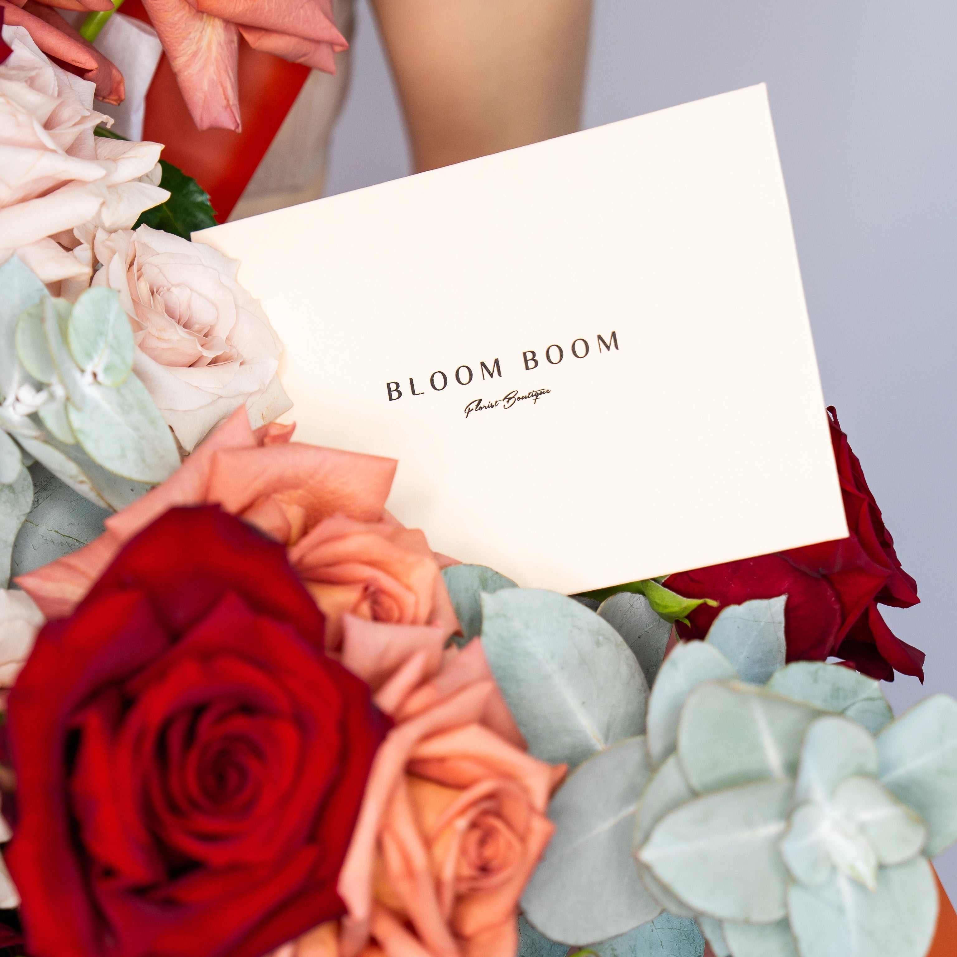 Bloom Boom Flowers business card nestled in luxury rose bouquet with red, peach and blush roses plus eucalyptus