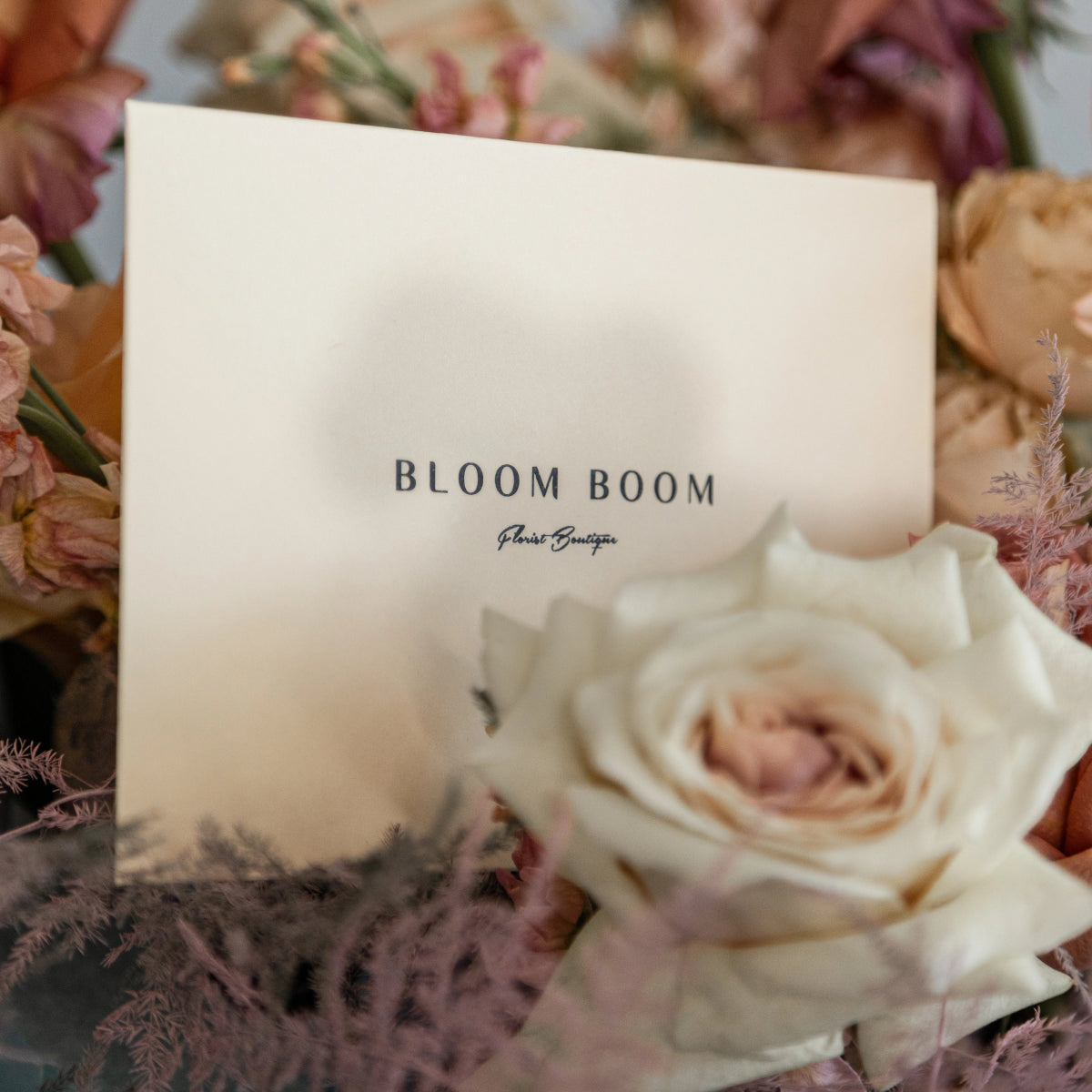 Bloom Boom Flower Boutique business card surrounded by soft pink and cream roses with purple dried flowers