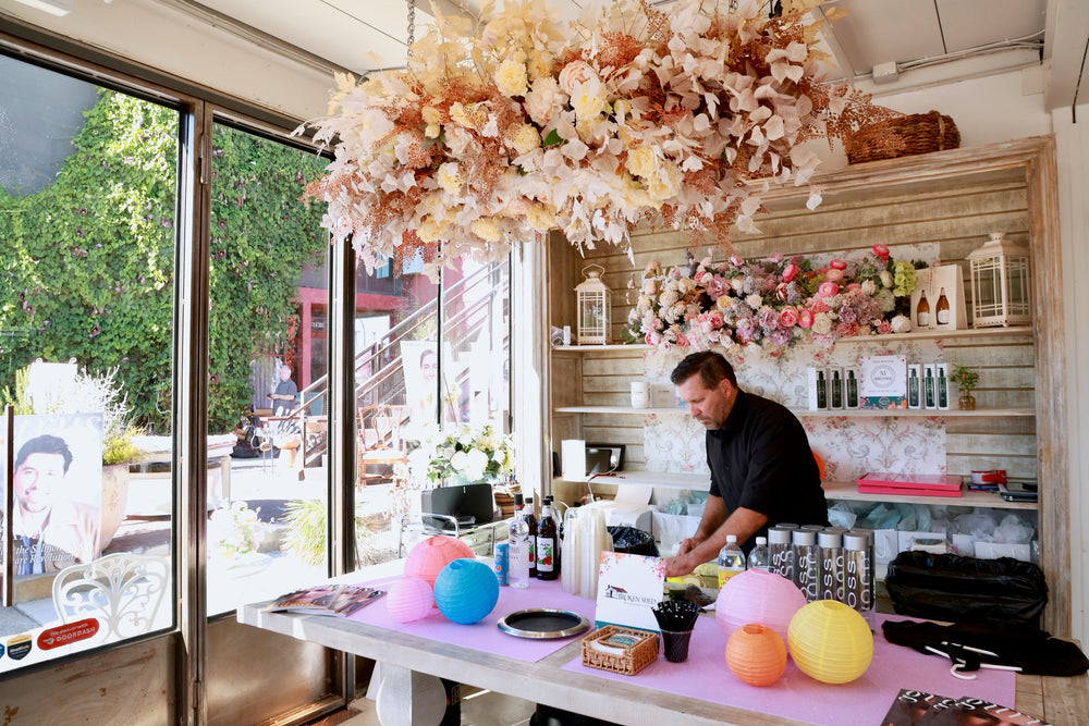 Bartender preparing drinks at a pink bar beneath a suspended dried floral cloud installation