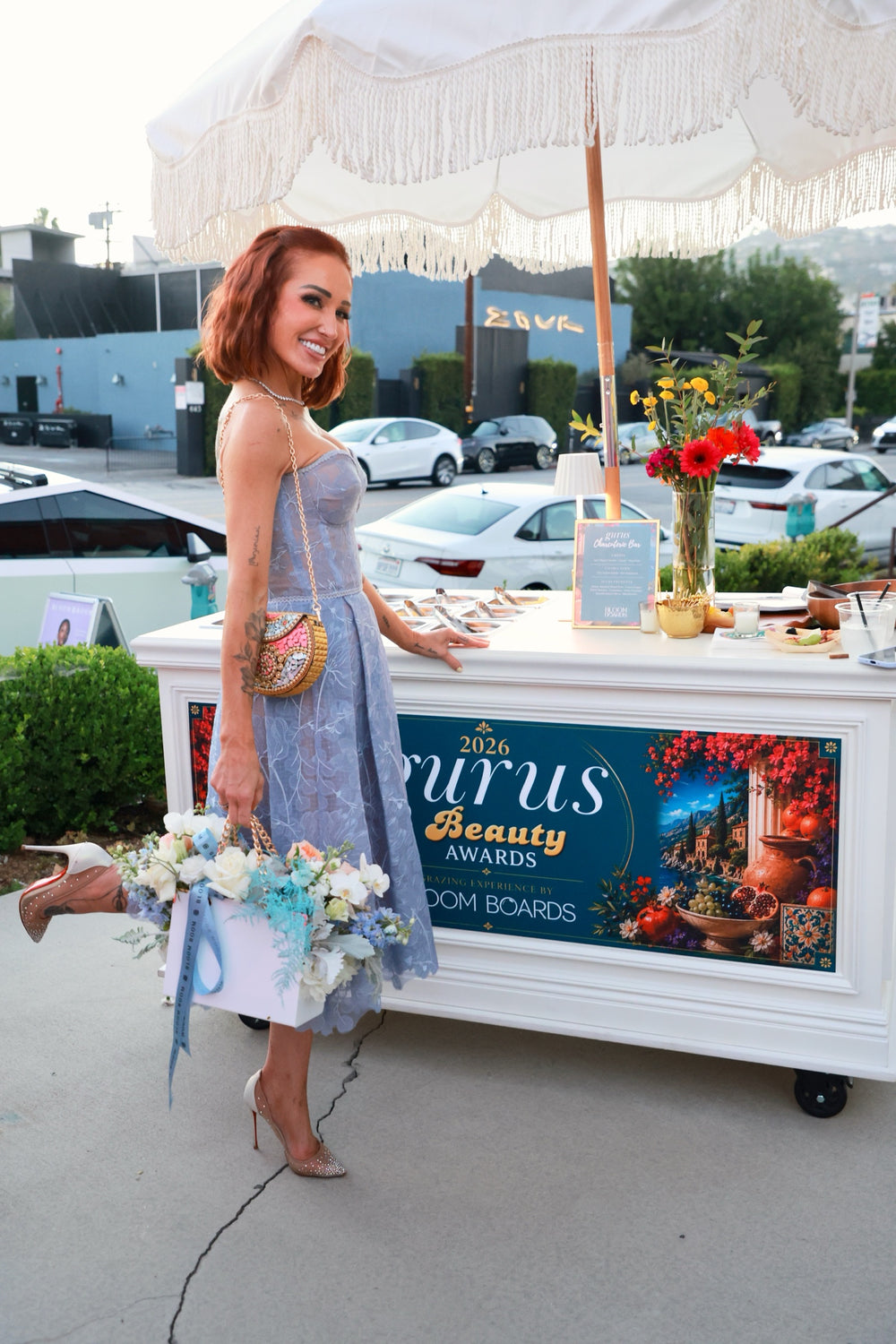 Guest posing beside the Gurus Beauty Awards flower cart with a bouquet at golden hour