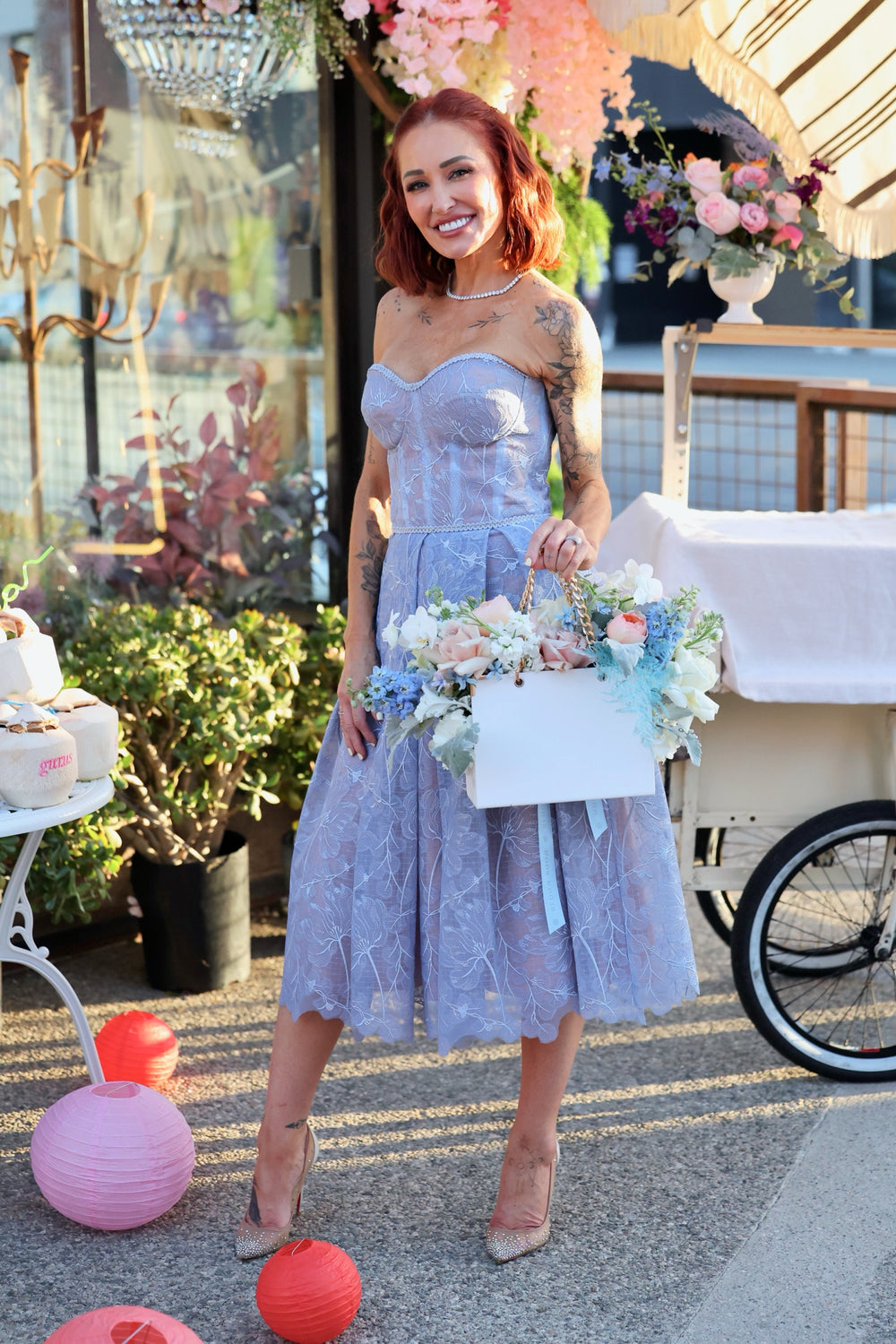 Guest in lavender lace holding a take-home flower bag arrangement outside the shop