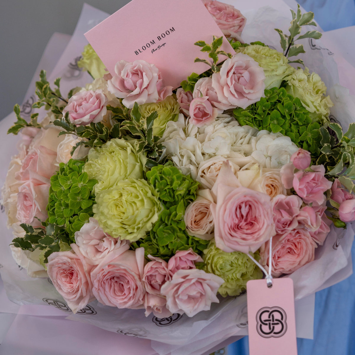 Luxury mixed flower bouquet with pink roses, green hydrangea, white tissue paper wrapping and Bloom Boom brand tag