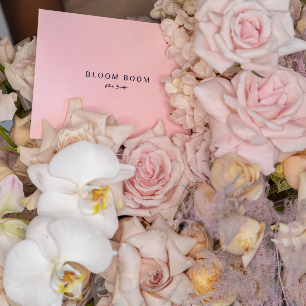 Pink Bloom Boom flower bouquet with blush roses, white orchids, and hydrangeas in wicker basket
