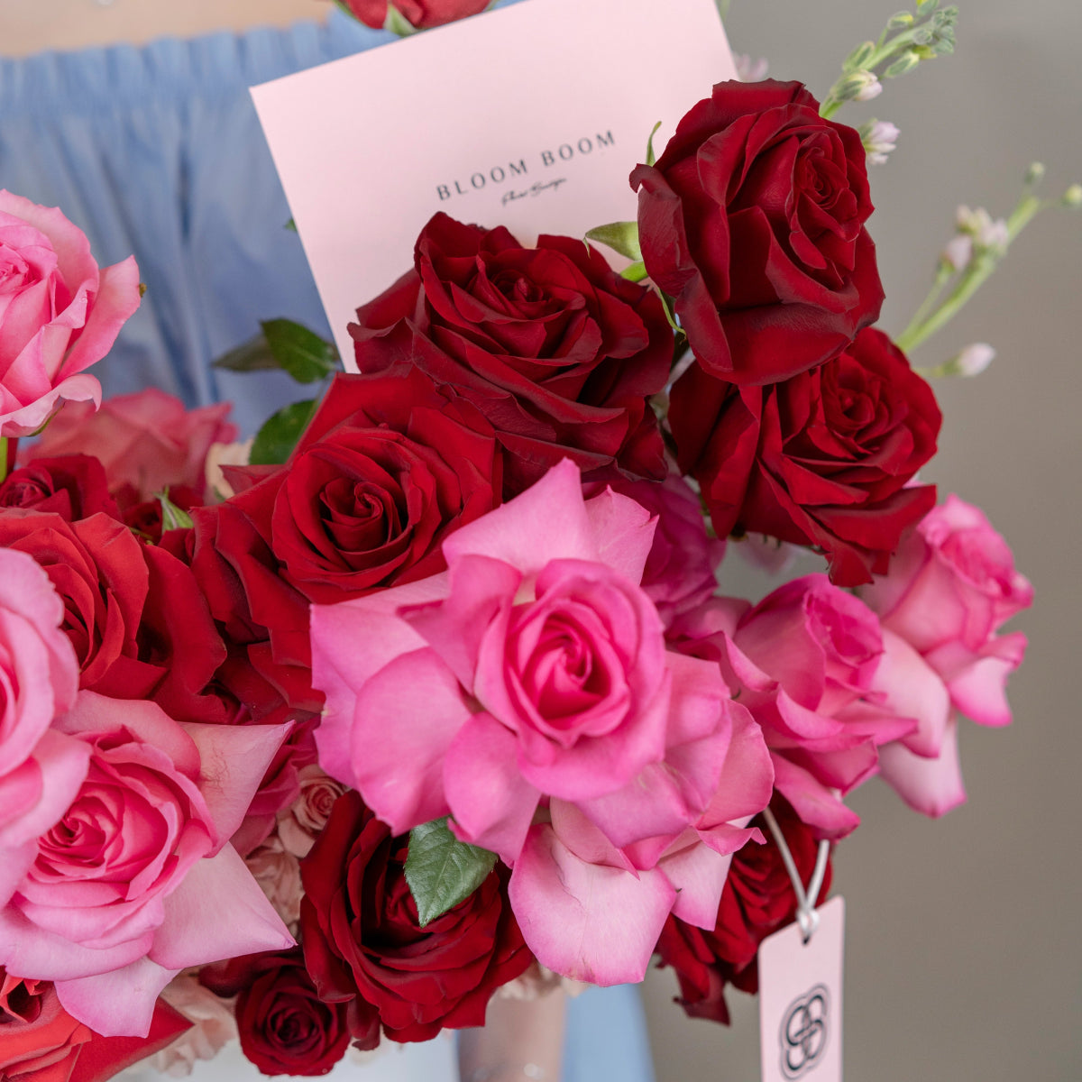 Bloom Boom branded flower bouquet with deep red and bright pink roses with green stems and white card
