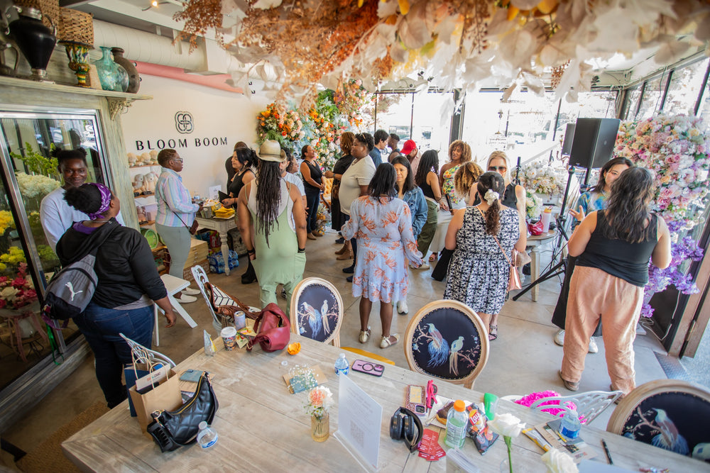 A full room of guests mingling under the dried floral ceiling installation beside the Bloom Boom sign