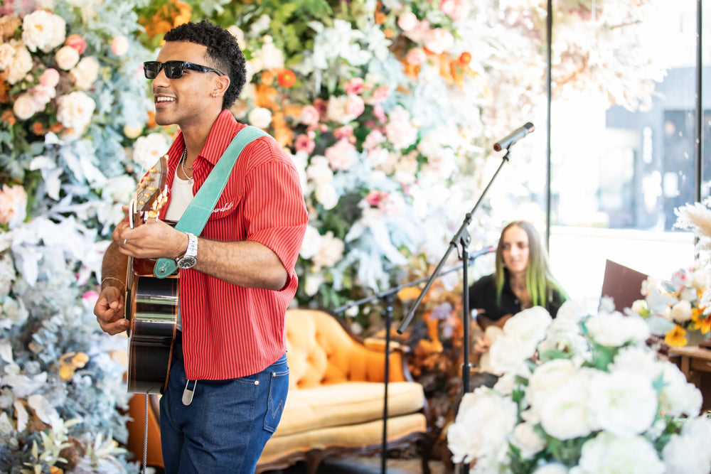 Guitarist and keyboardist performing against a lush floral backdrop with orange velvet sofa