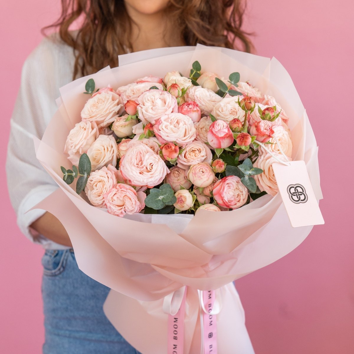 Blush pink and coral rose bouquet with eucalyptus wrapped in white paper, held against pink background