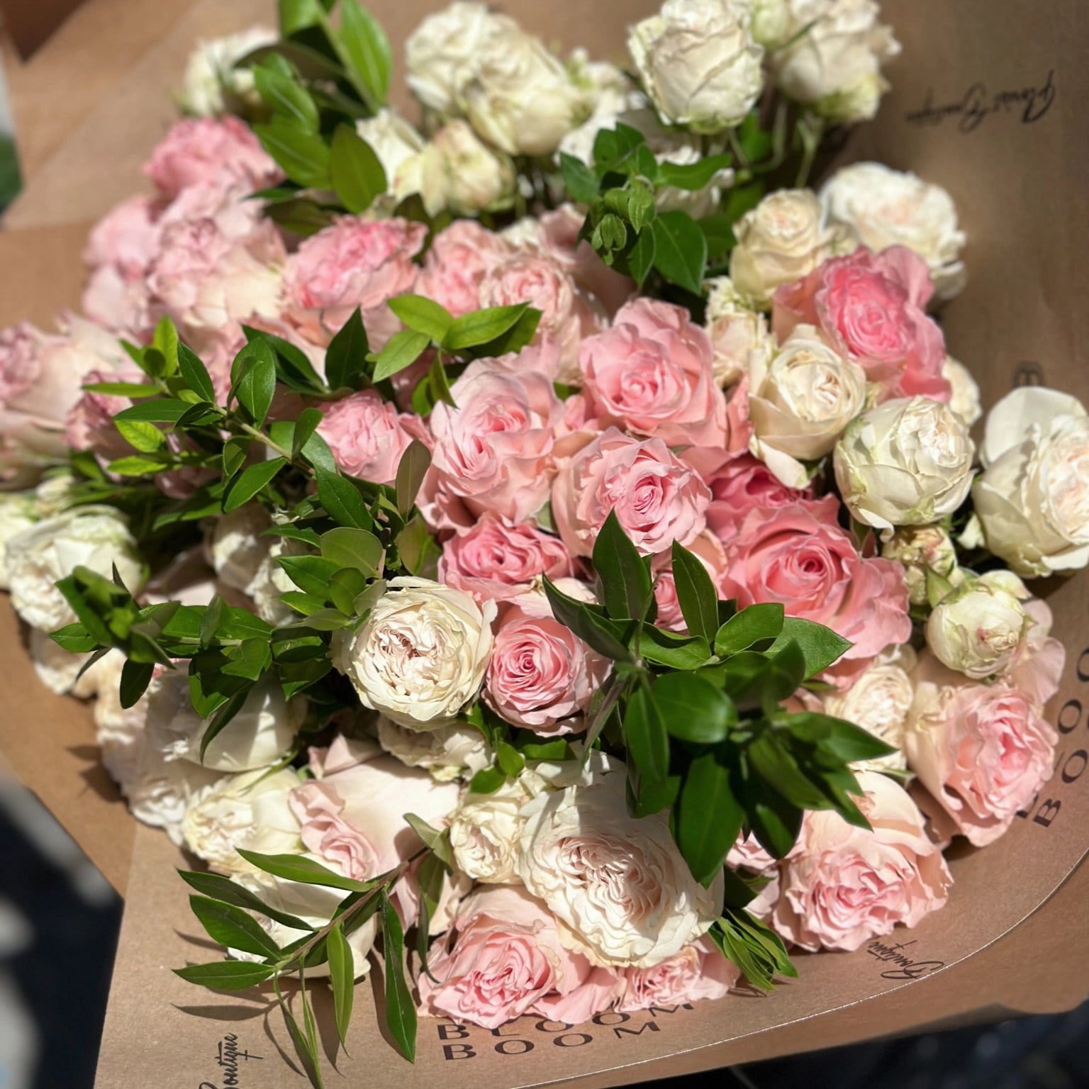 Blush pink and cream rose bouquet wrapped in brown kraft paper with green foliage accents from Los Angeles florist