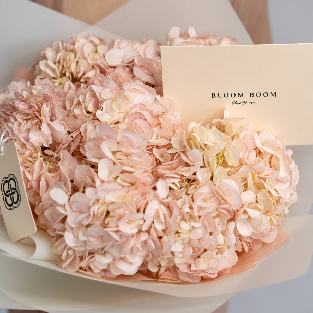 Elegant bouquet of blush pink hydrangea flowers wrapped in cream paper with Bloom Boom brand card