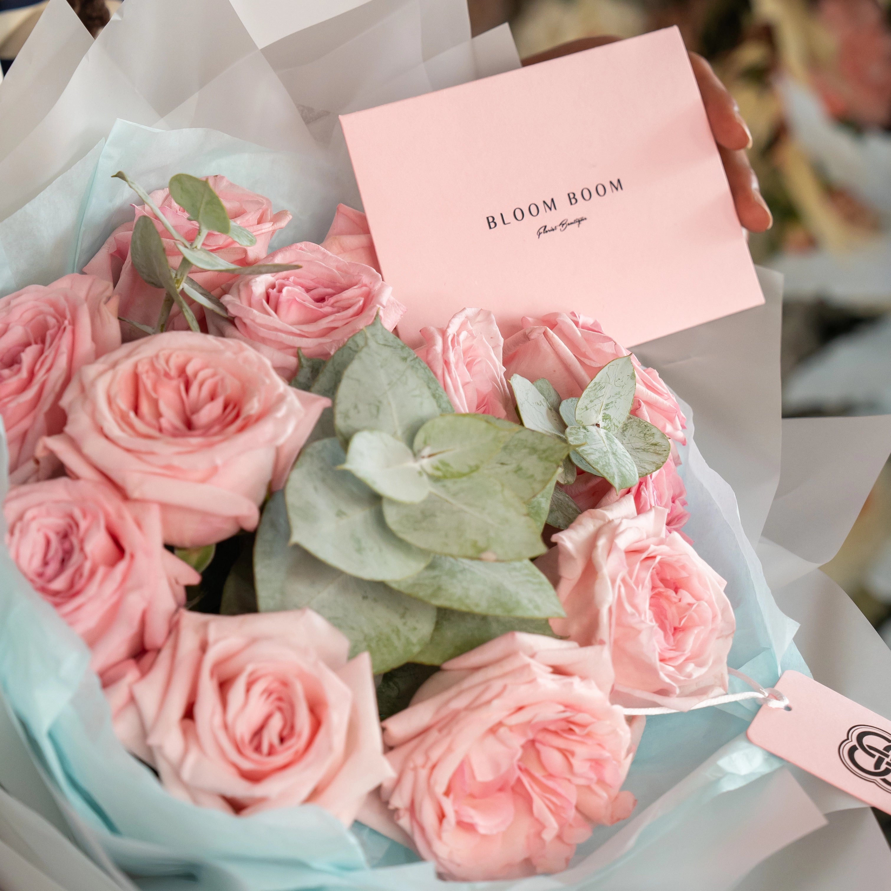 Blush pink rose bouquet with eucalyptus leaves wrapped in blue tissue paper featuring Bloom Boom florist branding