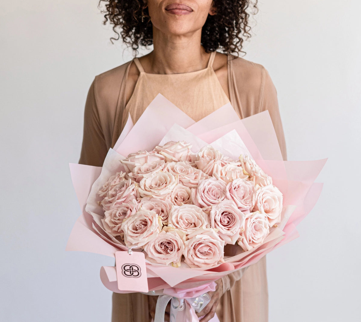 Woman holding large bouquet of 25 blush pink roses wrapped in soft pink paper with ribbon