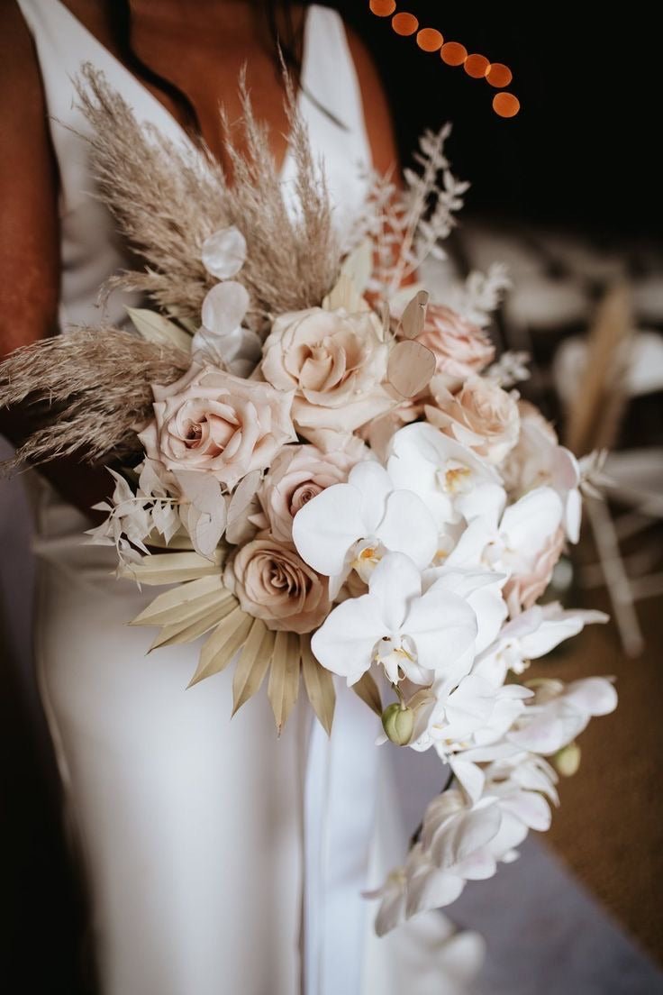Bridal bouquet with blush roses, white orchids, dried pampas grass and palm leaves in neutral tones