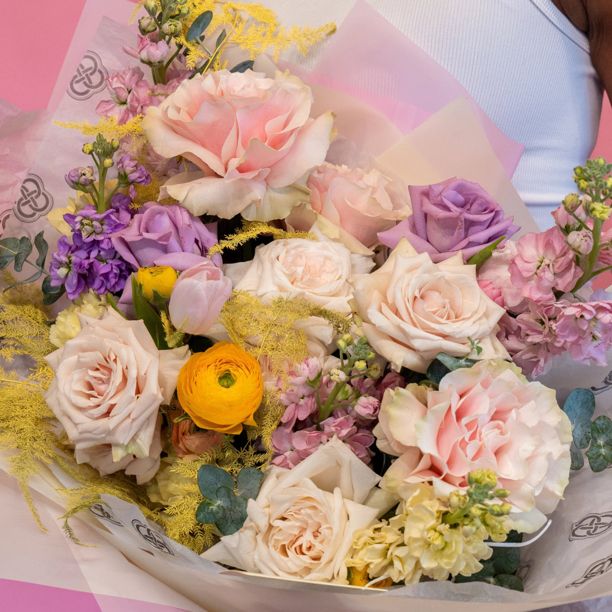 Mixed flower bouquet with blush pink roses, purple lavender roses, orange ranunculus and golden mimosa in white paper