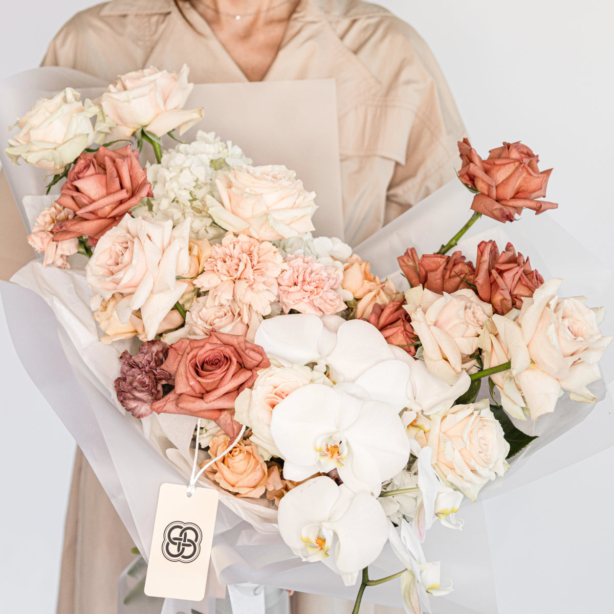 Mixed flower bouquet with coral roses, white orchids, pink carnations and hydrangea in white wrapping with gift tag