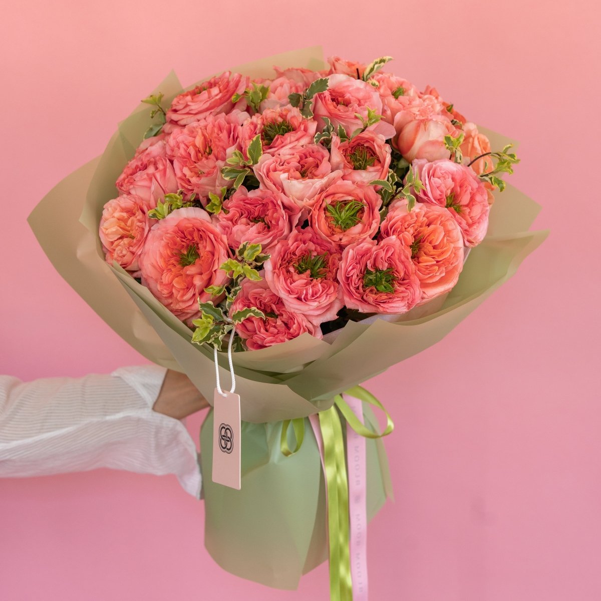 Coral pink ranunculus bouquet wrapped in beige paper with green ribbon on pink background