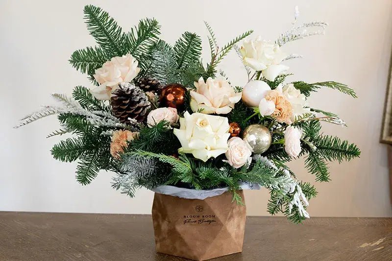 Holiday floral arrangement with white roses, pine branches, pinecones and ornaments in brown paper cube vase