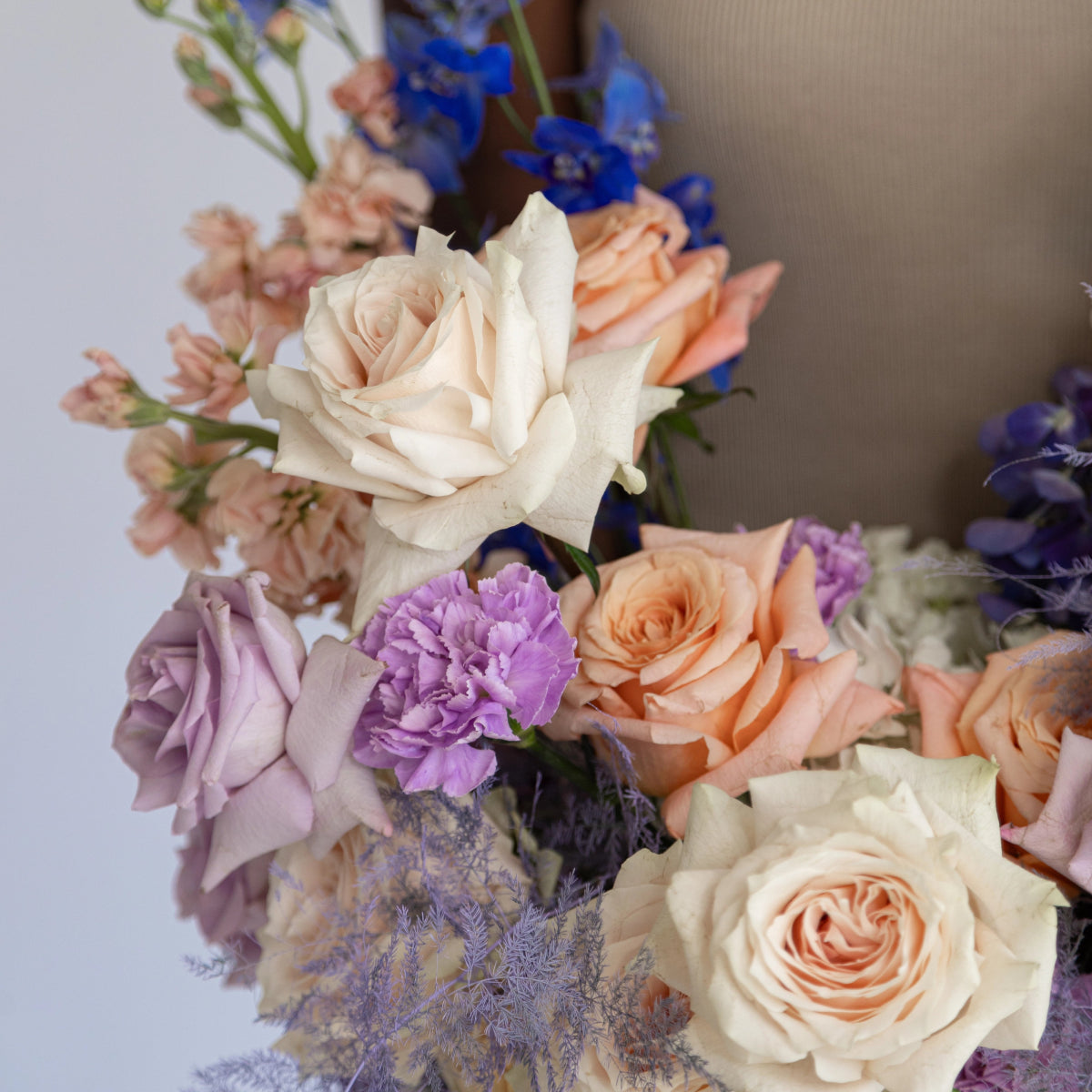 Mixed flower bouquet with cream and peach roses, purple carnations, blue delphiniums and dusty miller foliage