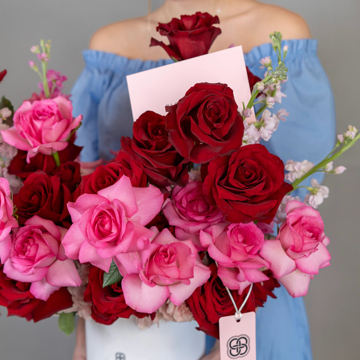 Mixed rose bouquet with deep red and pink roses, white baby's breath, held by woman in blue off-shoulder top