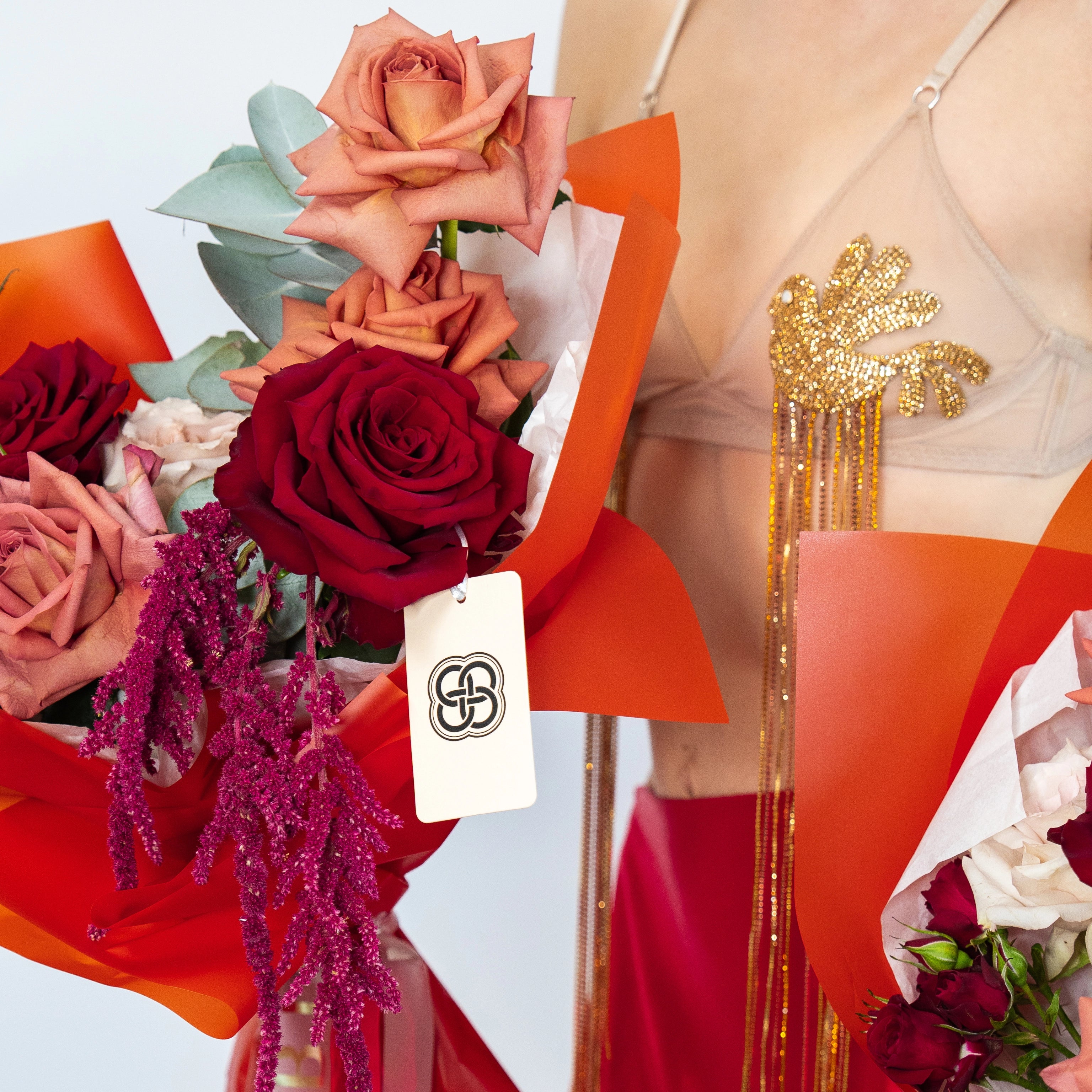 Mixed rose bouquet with burgundy and coral roses, eucalyptus leaves, wrapped in bright orange paper with white tissue