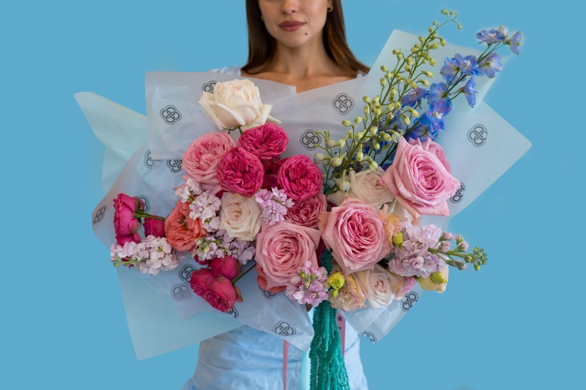 Mixed rose bouquet with pink, white, cream roses, purple delphinium in white tissue paper with green ribbon