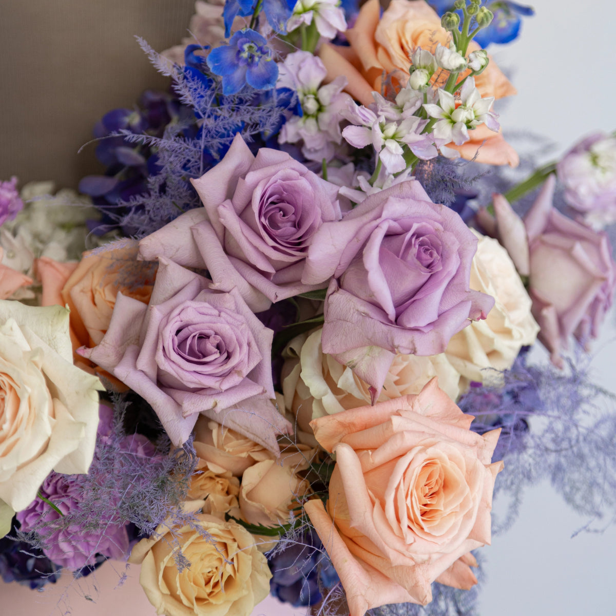 Mixed rose bouquet with lavender purple, peach coral and cream roses with blue delphinium and dusty miller foliage