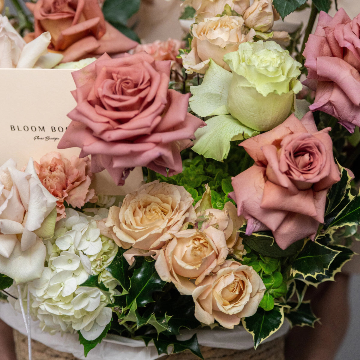Mixed flower bouquet with dusty pink roses, cream roses, white hydrangeas and green foliage in elegant arrangement