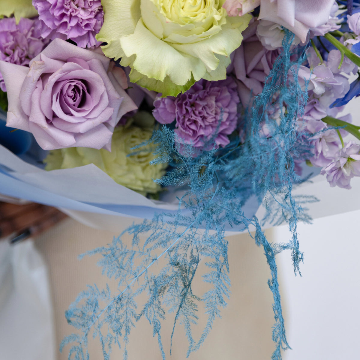 Purple roses and carnations with cream ranunculus and blue dried pampas grass in white wrapped bouquet