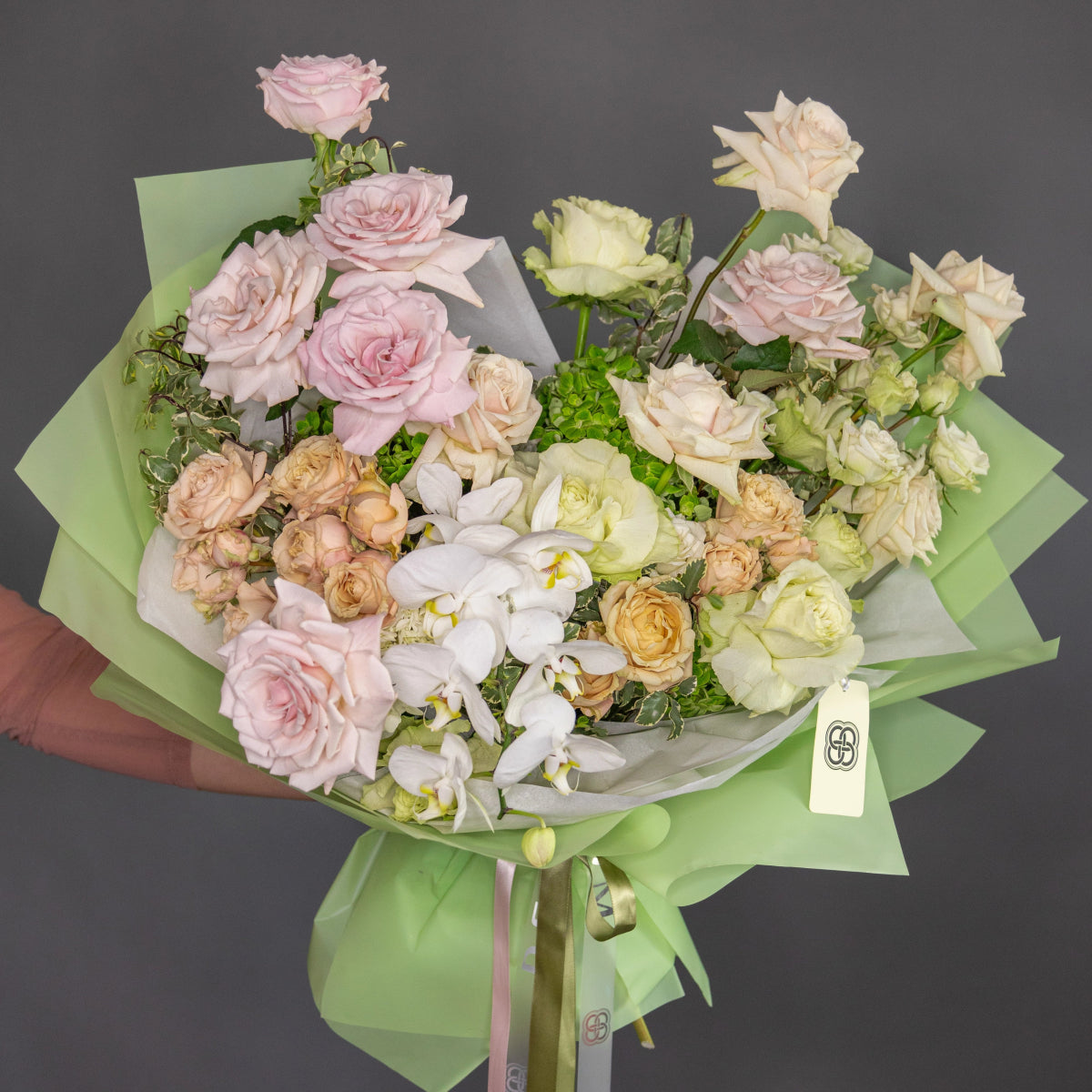 Pastel bouquet with pink roses, white orchids, cream flowers in sage green wrapping paper with ribbon