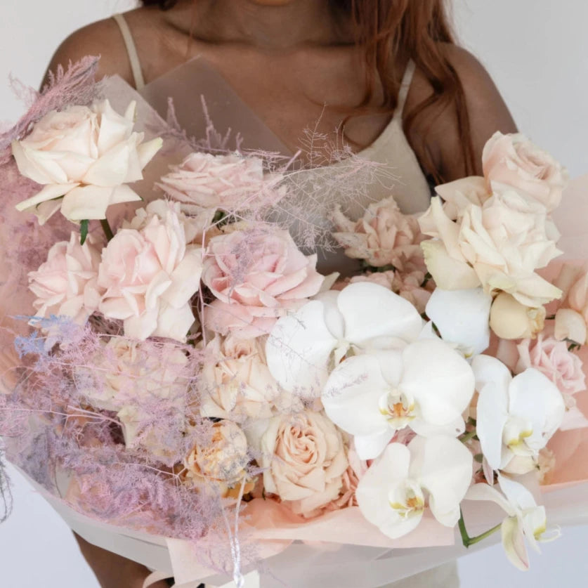 Pastel pink and white flower bouquet with orchids, roses, and hydrangeas wrapped in clear cellophane